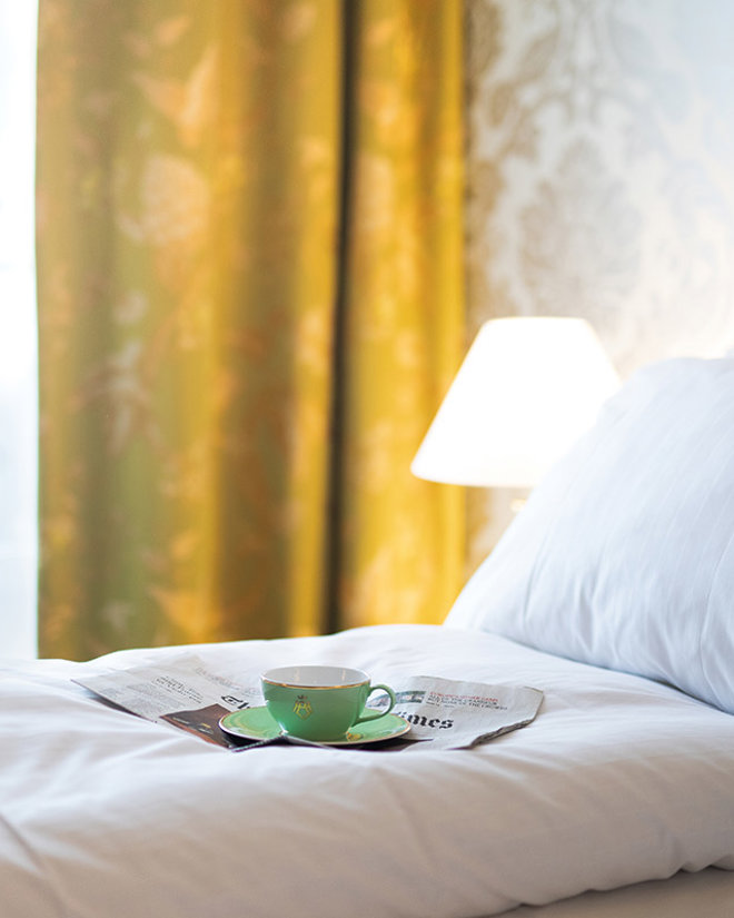 Oppredd seng med kaffekopp og avis på toppen på et hotellrom på Hotel Bristol.